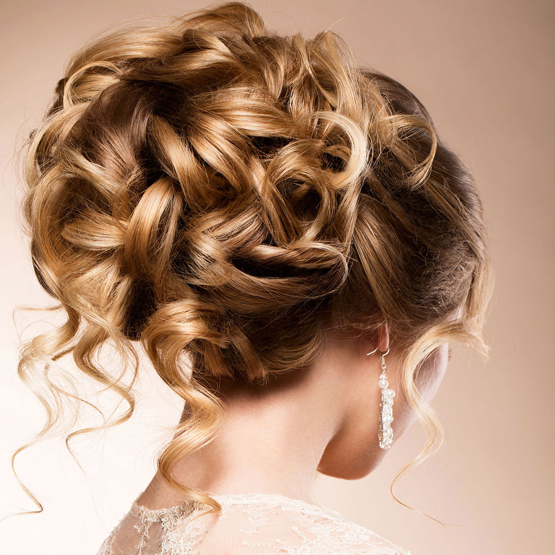 Close-up van bruidskapsel schuin van achteren, blond haar met highlights met slagen en krullen opgestoken.