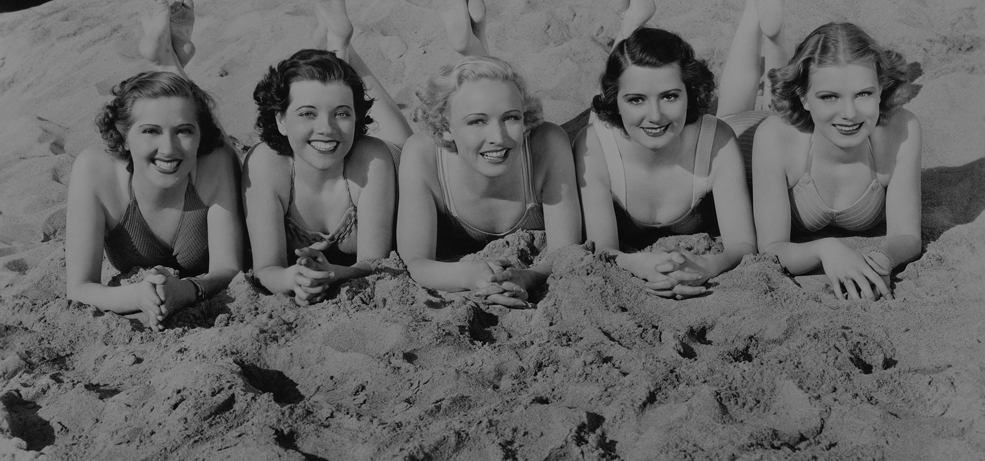 Portet van vijf jonge vrouwen met een retro en vintage finger waves kapsel liggend op het strand en glimlachend.