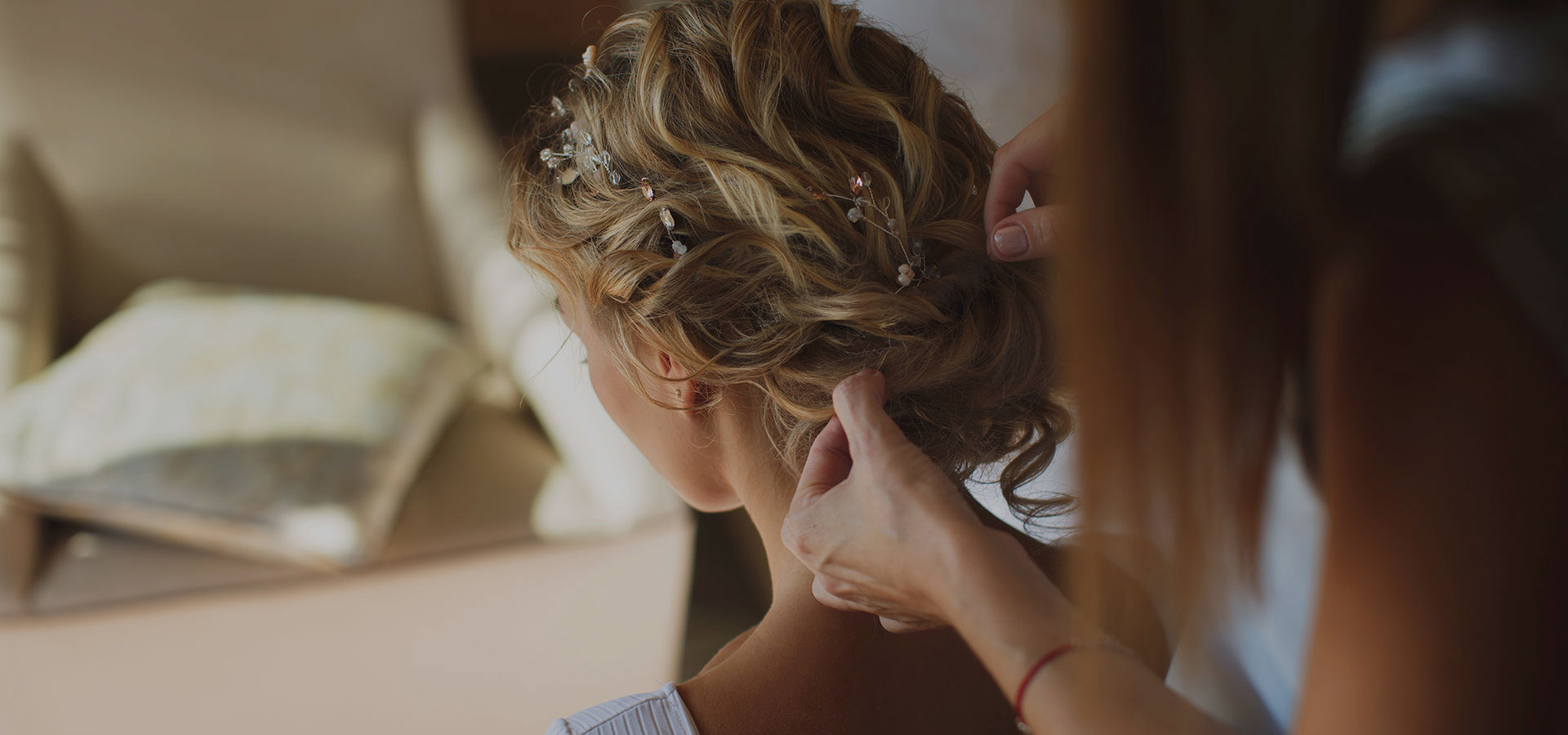 De kapper aan de slag met een Bohemian bruidskapsel van blond opgestoken haar met slagen en krullen, hairpins en haarsieraden.