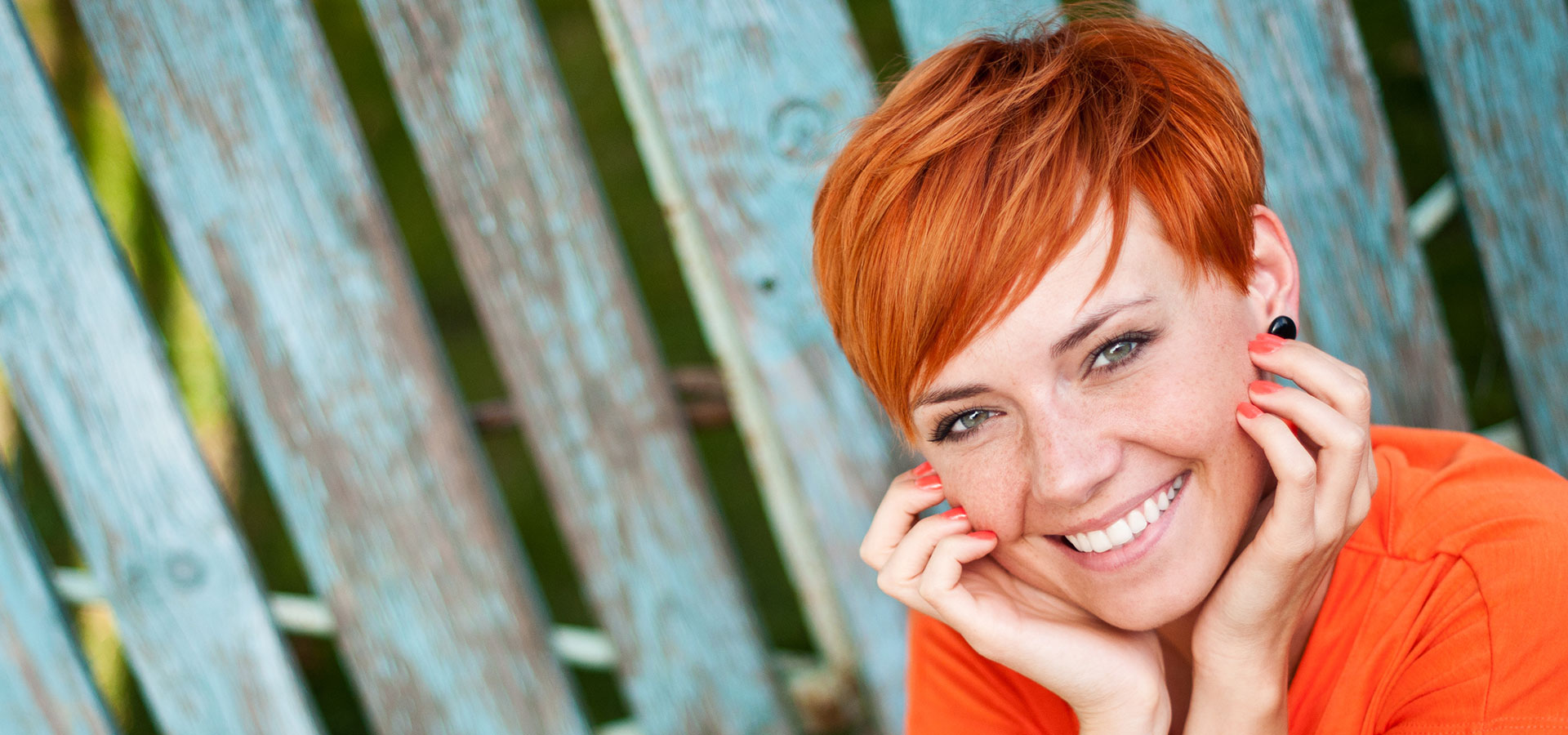 Stralende jonge vrouw met krachtig oranjerood kort haar heeft modern stijlvol kapsel laten knippen en zit buiten te genieten van de zomer.