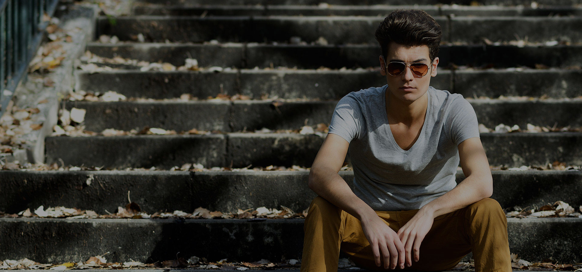 Jongeman met trendy herenkapsel in vintage style buiten zittend met zonnebril op brede stenen trap.